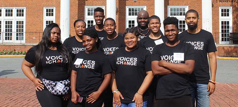 A group of SchoolTalk youth and staff in matching Voices of Change shirts in front of an academic building.